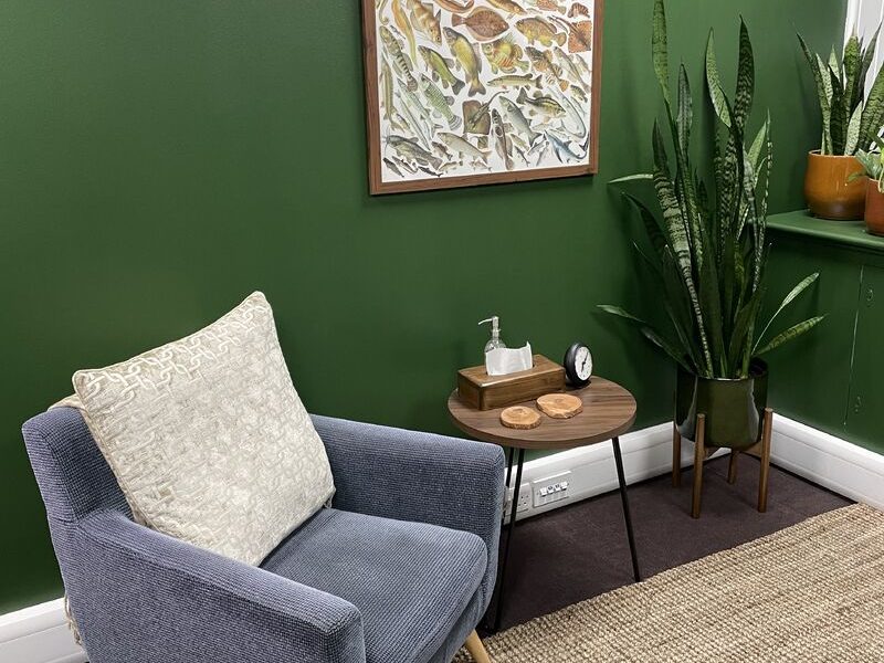 Another view of the Token House room: an armchair, a side table and plants against a deep green wall